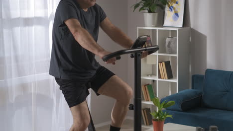 middle-aged-person-is-using-modern-exercise-bike-for-training-at-home-spinning-pedals-in-his-apartment-at-weekend-keeping-fit-and-health
